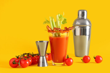 Glass of bloody mary cocktail with bacon and celery on yellow background