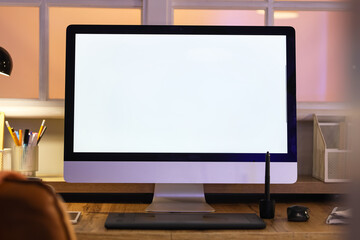 Workplace with blank computer monitor in office at night