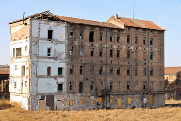 Side of an old brick building with many windows, one empty one boarded, with a faded old exterior....