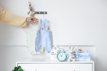 Young mother hanging baby clothes on light wall in stylish children's room