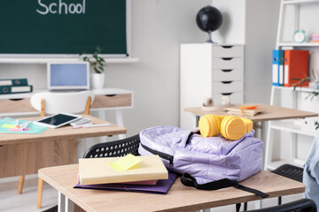 Lilac backpack with headphones and books on desk in classroom