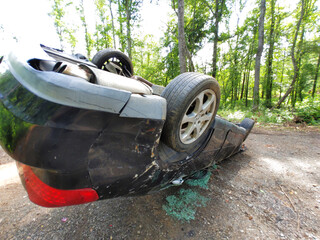 Damaged vehicle is flipped on its side along wooded dirt path, with vehicle collision