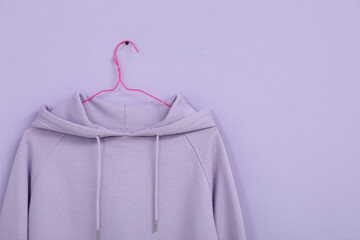 Hanger with stylish lilac hoodie on color background