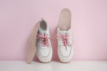 Sneakers with orthopedic insoles on bench near pink wall