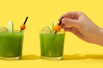 Female hand with glasses of green bloody mary cocktail garnished with physalis berries and lime on...