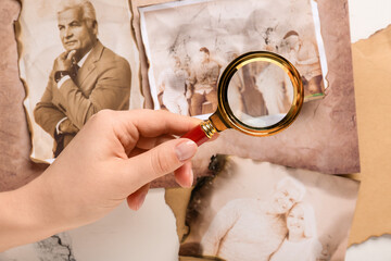 Female hand with magnifier and old photos of relatives. Concept of family tree
