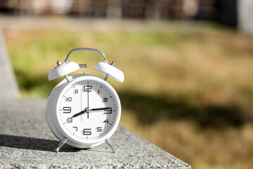 White alarm clock on concrete outdoors, closeup