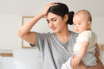 Tired mother suffering from postnatal depression with her baby in bedroom