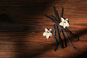 Vanilla sticks and flowers on wooden background, top view