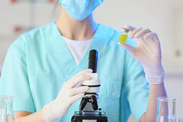Female scientist with ampoule and microscope in laboratory, closeup
