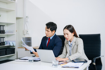 Two Asian professionals dealing with business stress and financial issues at office desk. Emotion, failure, frustration, teamwork under pressure.