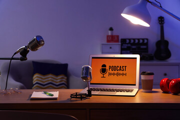 Podcaster's workplace with laptop, microphones and glowing lamp in dark studio