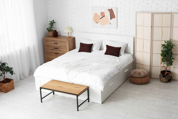 Interior of light room with big bed, folding screen and plants