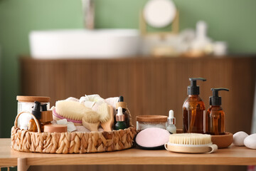 Wicker tray with different spa accessories and cosmetic products on wooden table in bathroom