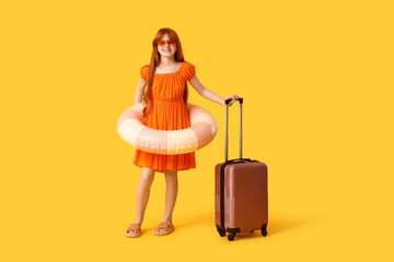 Cute girl with suitcase and inflatable ring on yellow background. Travel concept
