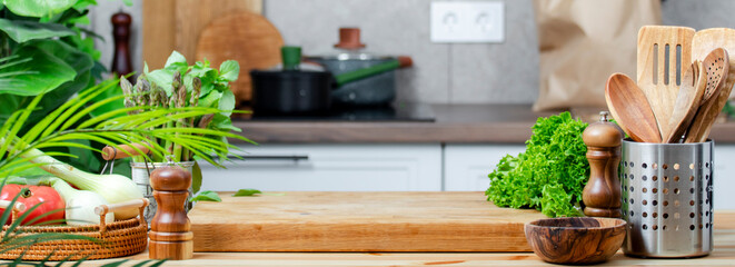 Fresh vegetables and cooking utensils arranged on a wooden table in a vibrant kitchen with plants and healthy ingredients