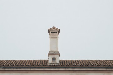 A lone chimney, standing tall against a muted sky, perched upon a traditional tiled roof, exuding a sense of quiet simplicity and classic architectural design.