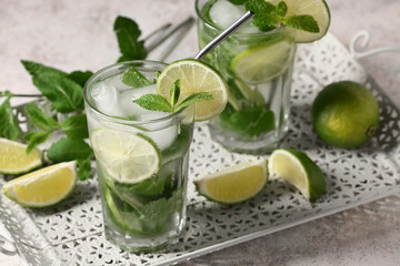 Tray with glasses of tasty mojito and ingredients on white grunge background, closeup