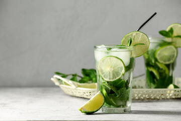 Glass of tasty mojito and piece of lime on grey background, closeup