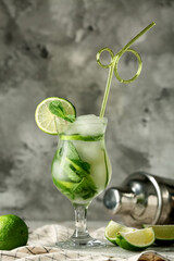 Glass of tasty mojito, napkin and lime on grey grunge background, closeup