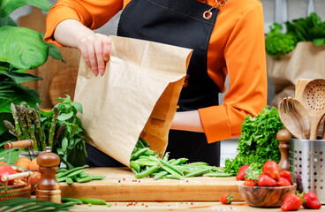 woman pours green peas out of a paper bag and prepares fresh vegetables for vegan meal in kitchen
