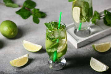 Glass of fresh mojito and pieces of lime on grey background, closeup