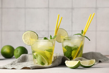 Glasses of fresh mojito and limes on table near grey tile wall, closeup