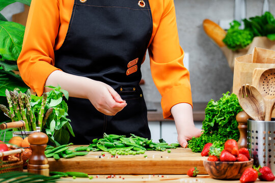 woman prepares colorful vegetables on a wooden cutting board, demonstrating healthy cooking in a well-equipped kitchen. - Powered by Adobe