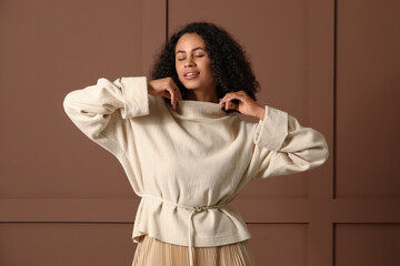 Stylish young African-American woman in sweater near brown wall