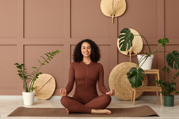 Sporty African-American woman meditating near brown wall