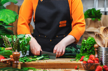 female chef skillfully chops green vegetables tuscan kale in a lively kitchen, showcasing a commitment to healthy vegan cuisine.