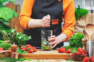 woman prepares a healthy refreshing drink in a lively kitchen, using fresh fruits and herbs while showcasing her cooking skills.
