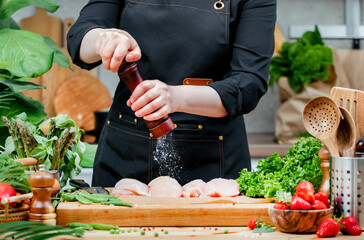 Woman chef holds raw chicken fillet preparing yummy dishes in a cozy kitchen with fresh herbs and...