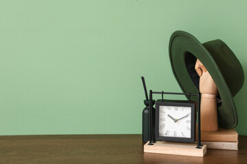Wooden hand with felt hat, clock and books on shelf near green wall
