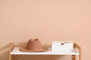 Stylish felt hat with box on shelf near beige wall