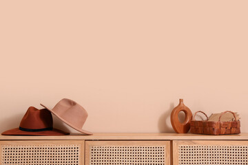 Stylish hats with books and vase on chest of drawers near beige wall
