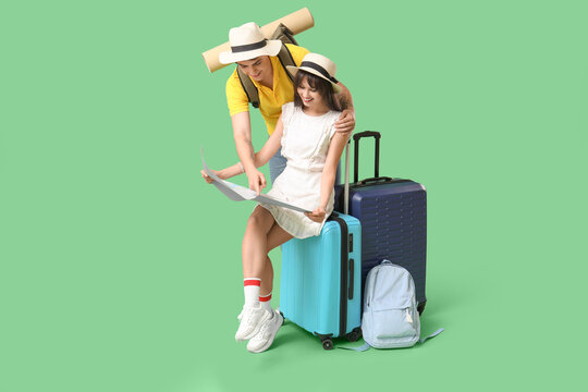 Couple of tourists with map and suitcases on green background