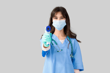 Female medical intern in mask with infrared thermometer on light background