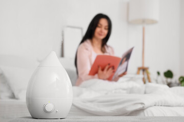 Air humidifier on bench against woman reading magazine in bedroom, closeup