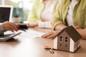 House model and key on table against real estate agent working with couple in office, closeup