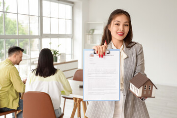 Female Asian real estate agent with agreement and house model against couple in office