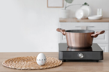 Modern kitchen timer and mini stove with cooking pot on table in room