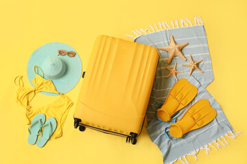 Composition with suitcase, swimsuit and beach accessories on yellow background