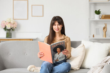 Smiling young woman reading fashion magazine on sofa at home
