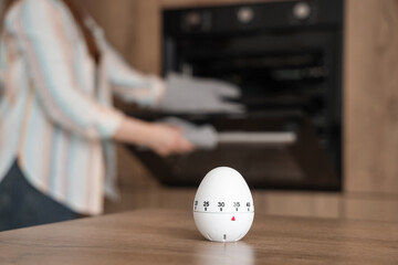 Kitchen timer on table against woman baking in room, closeup