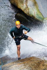 Latin american canyoneer rappelling down a waterfall, giving thumbs up while enjoying extreme sport