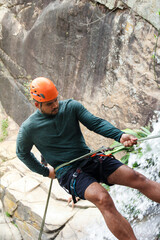 Adventurous latin american man carefully rappelling down a rocky waterfall, demonstrating skill and...