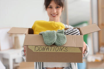Young woman holding box with clothes for donation in bedroom, closeup