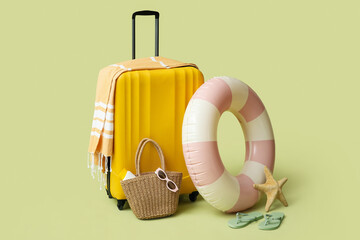 Inflatable ring, suitcase and beach accessories on green background, closeup