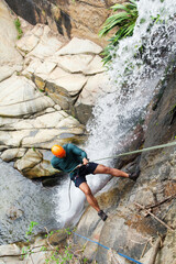 Latin american canyoneer rappelling down a waterfall in a rocky canyon, enjoying extreme sport and...